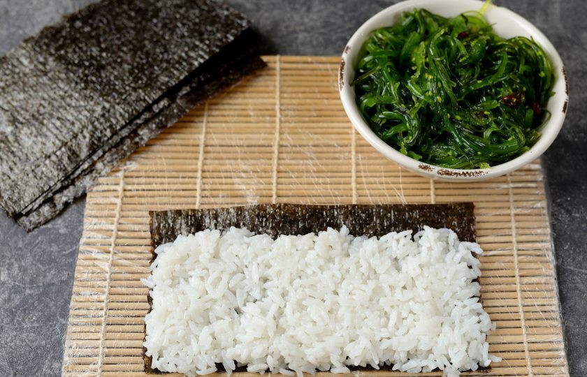 1. Этап. Роллы с чукой: Лист нори разрежьте пополам. Смачивайте руки и ложку в воде, выкладывайте рис на нори, оставив дальний край на 1 сантиметр свободным.