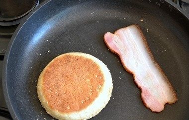 1. Этап. Яичница по-бенедиктински: 5. На сухую сковороду положить нижнюю часть булочки, разрезанной пополам, и ломтик бекона. Обжарить до золотистой корочки.