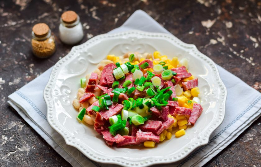 1. Этап. Салат с кукурузой, колбасой и фасолью: Зеленый лук ополосните и просушите, нарежьте мелко и добавьте в салат.