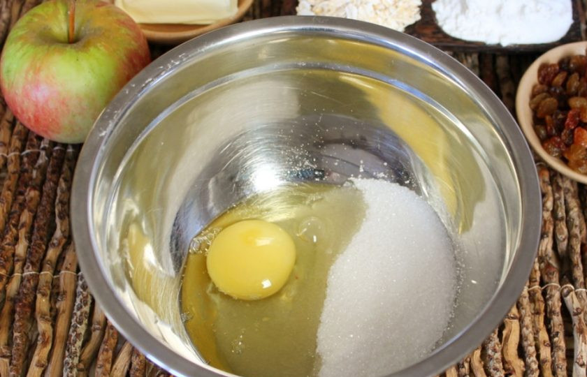 1. Этап. Овсяное печенье с изюмом и яблоками: В миску насыпаем сахар и добавляем яйцо, все взбиваем венчиком.