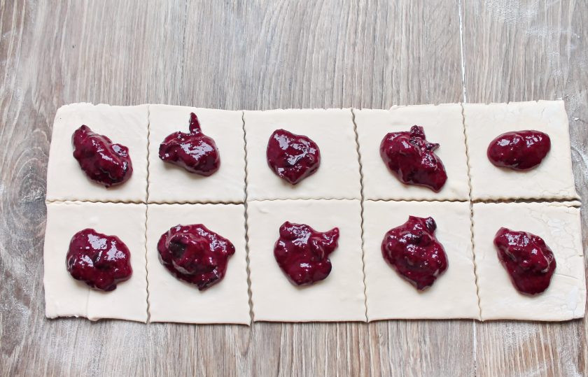 1. Этап. Конвертики с джемом из черной смородины: Слоеное тесто немного раскатайте в одном направлении и разрежьте на квадратики. Выложите на середину каждого квадрата джем.