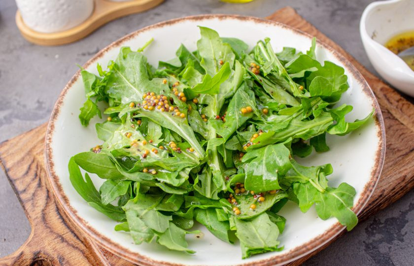 1. Этап. Салат Нисуаз с рукколой: На тарелку выложите листья рукколы и полейте 1/3 частью приготовленного соуса.