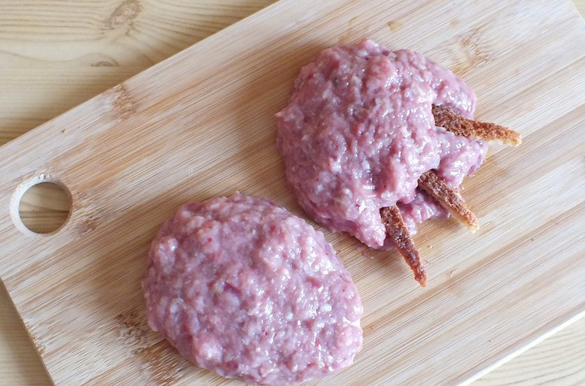 1. Этап. Котлеты Медвежьи лапы: По истечении времени достаньте из холодильника чашу с фаршем. Разделите его на 5-6 частей. Руки смажьте растительным маслом. На ладони распределите часть фарша, придайте ей слегка усеченную форму. С одной из сторон вставьте хлебные 