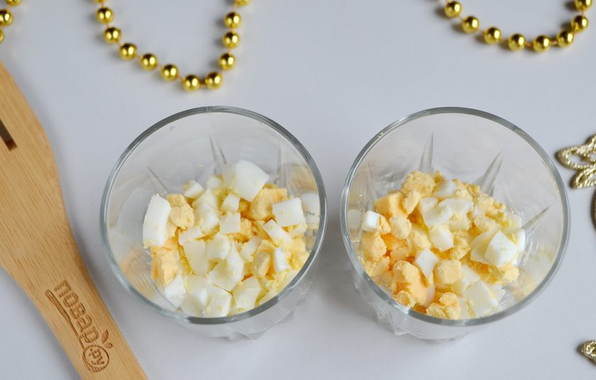 1. Этап. Новогодний салат в стакане за 5 минут: Возьмите прозрачные стаканы. На дно положите рубленые яйца. Майонез.