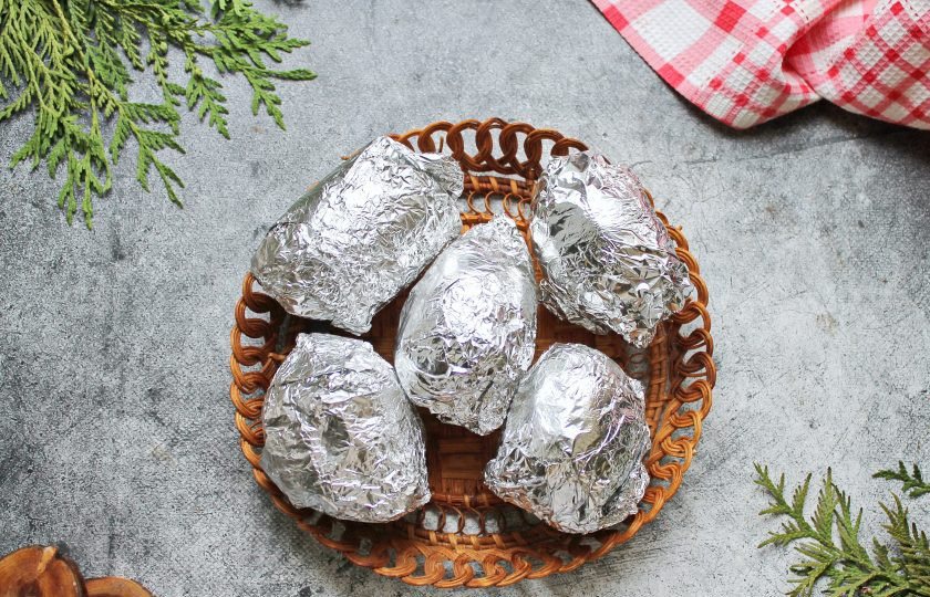 1. Этап. Запеченный картофель с беконом и сыром: Картофель тщательно вымойте щеткой в теплой воде от земли и грязи. Каждый чистый клубень заверните в два слоя и выложите на противень. Поставьте картофель в горячую духовку и готовьте при температуре 200 градусов в течение 50-60 минут, до готовности картофеля. Готовый картофель достаньте и дайте ему полностью остыть.