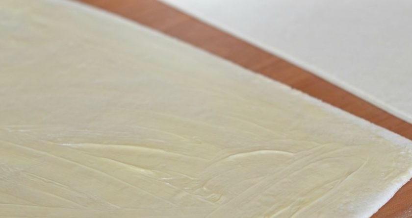 1. Этап. Слоеное тесто без яиц: Сливочное масло предварительно достаем, чтобы оно немного растаяло. Смазываем тесто маслом по всей поверхности равномерно, сверху выкладываем второй слой теста так, чтобы совпали края.