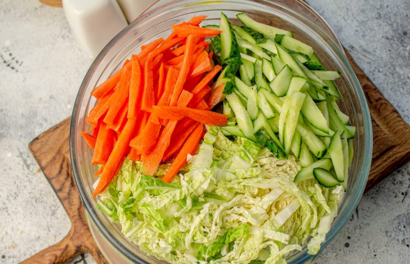 1. Этап. Салат по-китайски Харбинский: Пекинскую капусту (только верхнюю часть) нарежьте на тонкие длинные полоски. Морковь очистите и нарежьте соломкой, также соломкой нарежьте огурец. Добавьте овощи к рисовой лапше.