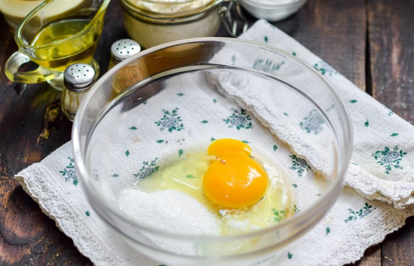 1. Этап. Вкусные и пышные оладушки: В миску всыпьте ложку сахара и вбейте куриное яйцо.