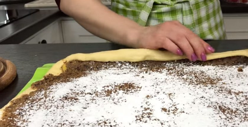 1. Этап. Рулет с черносливом и орехами в медовой корочке: 6. Выложите начинку ровным слоем, отступая от каждого края теста по 3 см. Посыпьте начинку сахарной пудрой и скатайте рулет. Переложите рулет на покрытый пергаментом противень.