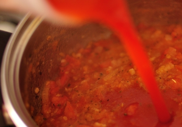 1. Этап. Тефтели с начинкой: Оставшийся чеснок и репчатый лук мелко нарезаем. В сковороде разогреваем 2 столовые ложки масла и обжариваем на нем лук и чеснок до прозрачного состояния. Пока они жарятся, мы измельчаем помидоры до состояния пюре при помощи блендера, добавляем их в сковороду и тушим в течение 5 минут. Потом вливаем томатный сок, добавляем сушеный базилик, соль и перец, тщательно перемешиваем все, и доводи до кипения.