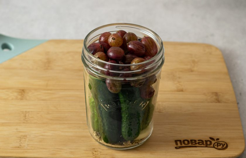 1. Этап. Маринованные огурцы с крыжовником: Свободное пространство заполните крыжовником. Влейте в банку горячую воду, прикройте крышкой и оставьте на 10 минут.