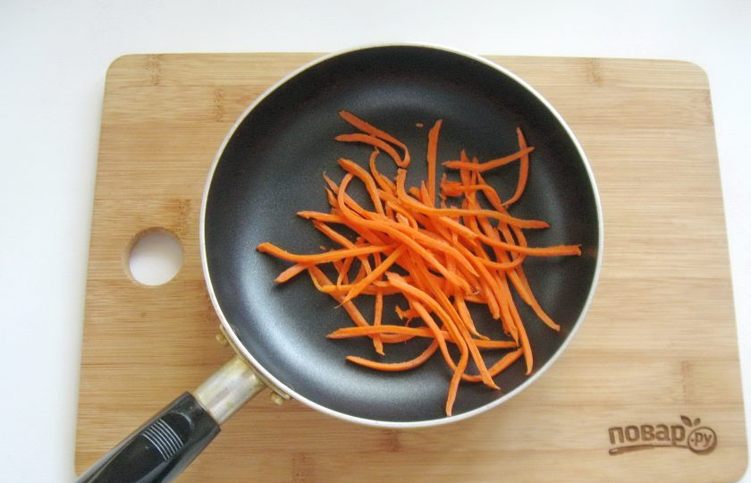 1. Этап. Кальмары с луком на сковороде: Морковь очистите, помойте и нарежьте соломкой. Выложите в сковороду.