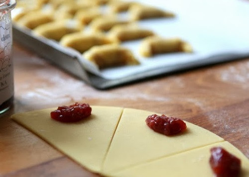 1. Этап. Рогалики из песочного теста: 1. Муку просейте в миску, разотрите с маслом и сахаром. Добавьте сметану, желтки. Взбейте миксером или хорошенько вымешайте ложкой. Поделите на 3 части и отправьте в холодильник на часа 2-3. По истечении указанного времени одну часть выберите. Раскатайте тонко (толщина 2-3 мм), сверху положите большую тарелку, вырежьте круг, затем разделите его на 8 частей. В центр широкой части треугольника выложите по ложке начинки.