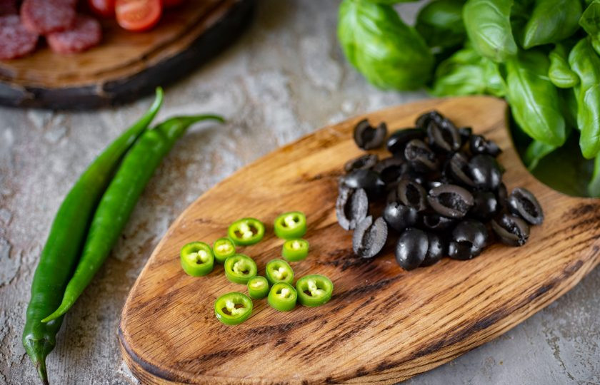 1. Этап. Мексиканская острая пицца: Каждую маслину без косточки также разрежьте на две половинки, а перчик чали нарежьте тонкими колечками, по ходу удаляя семена.