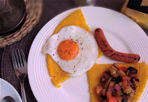 1. Этап. Кукурузная лепёшка из поленты: Приготовлю глазунью и погрилю сосиску. Подаём. Режем лепёшку на 4 части. По 2 ломтя каждому. Выкладываем на одну глазунью, на другую - овощи и помещаем на тарелку сосиску.