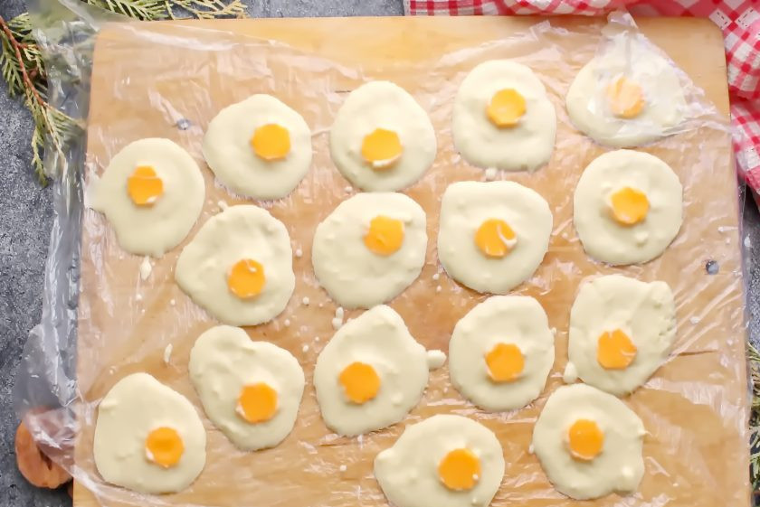 1. Этап. Конфеты Яичница: Противень или разделочную доску застелите пергаментом и разложите шоколад по одной столовой ложке. Выложите на каждую порцию шоколада по одной круглой конфетке и немного утопите ее. Уберите в прохладное место до застывания.