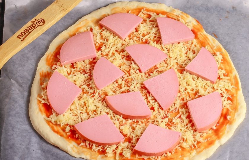 1. Этап. Пицца «Семейная»: Присыпьте основу половиной массы натертого сыра и выложите нарезанную колбасу.