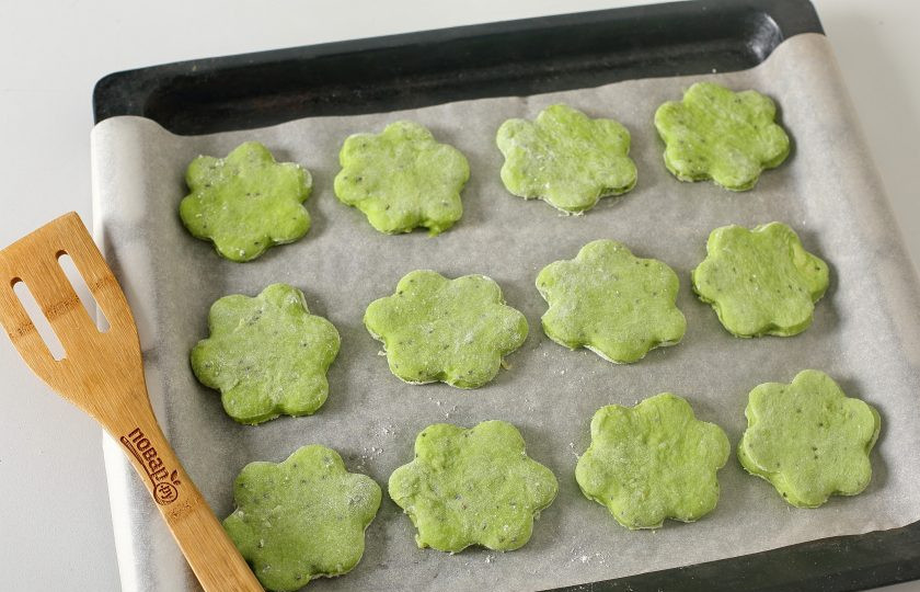 1. Этап. Печенье с киви: Рабочую поверхность присыпьте мукой, раскатайте тесто толщиной 4-5 мм. и вырежьте формочкой печенье в виде цветка. Переложите заготовки на противень, застеленный пергаментом.