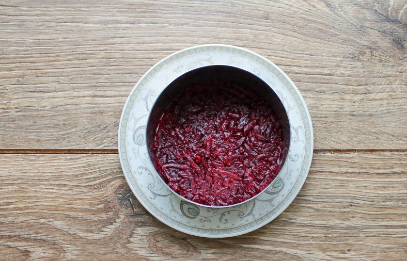 1. Этап. Салат Красный бархат из свеклы с творогом: Натертую свеклу хорошенько отожмите от сока. Сервировочное кольцо установите на блюдо и выложите 1/3 натертой свеклы, прижмите ложкой.