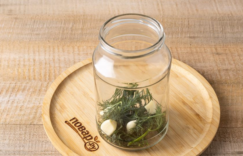 1. Этап. Цветная капуста маринованная с огурцами на зиму: В чистую стерилизованную банку выложите зелень и чеснок.