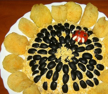 1. Этап. Салат Подсолнух с курицей: Маслины разрезаем на 4 части и украшаем ими салат, они будут семечками подсолнуха, а по центру немного желтков.