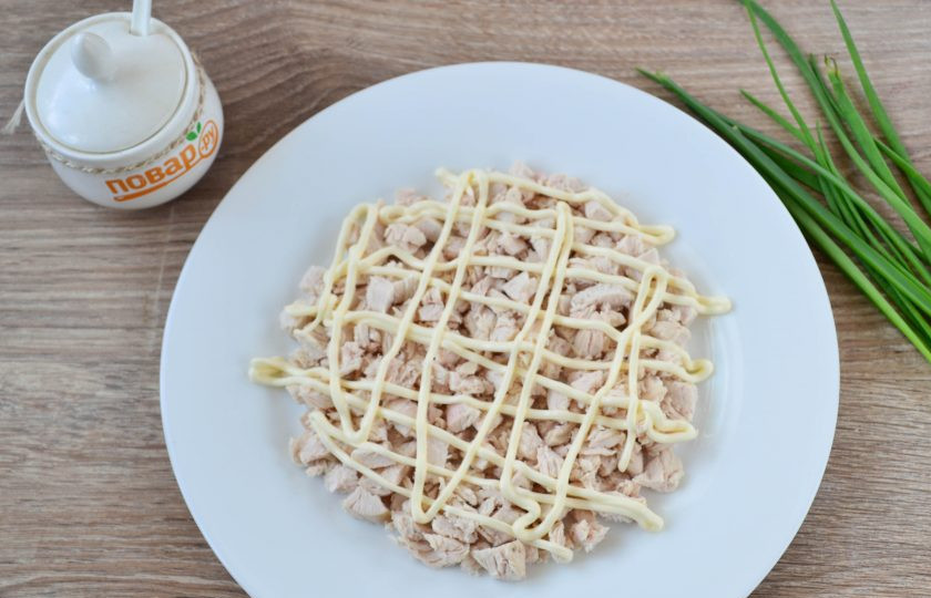 1. Этап. Салат Солнышко на Пасху: Куриную грудку мелко нарежьте и выложите первым слоем. Сверху смажьте майонезом. Очень удобно покрывать салаты сеточкой из майонеза, для этого необходимо или сделать маленький надрез на пачке майонеза, или переложить необходимое количество майонеза в одноразовый кондитерский мешок и сделать на нем надрез.