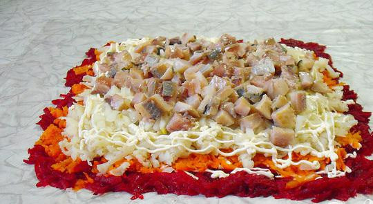 1. Этап. Рулет с сельдью на Старый Новый год: 5. Маринованный лук выкладываем на картофель, потом - сельдь. Выкладываем сельдь на середину слоя. Края пленки приподымаем, свертываем рулет, закрепляем края и укладываем на доску. Для скрепления и пропитки слоев часа на три убираем рулет в холодильник.