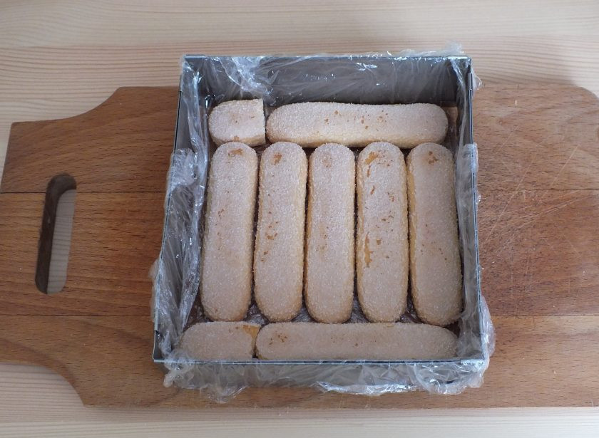 1. Этап. Торт из печенья савоярди: Возьмите разъемную форму, выложите ее пищевой пленкой и уложите первый слой из печенья. Смочите слегка соком от консервированных ананасов.