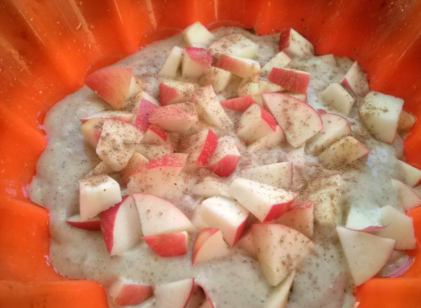 1. Этап. Вегетарианская шарлотка без яиц: Силиконовую форму сбрызните водой. Выложите в неё половину теста и нарезанные яблоки, посыпьте корицей.