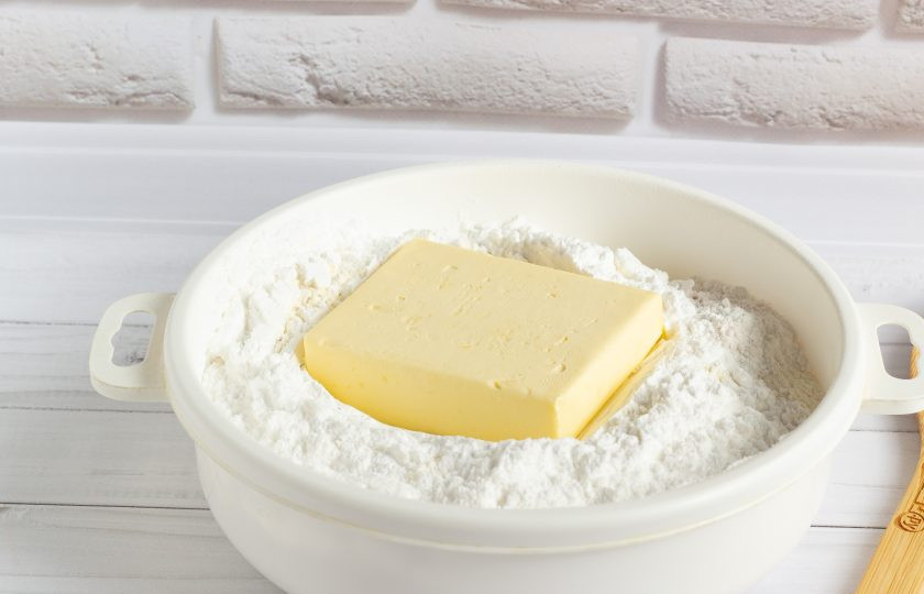 1. Этап. Яблочный пирог по-польски: В сухую миску просейте муку, сахарную пудру и разрыхлитель. Добавьте холодное сливочное масло.