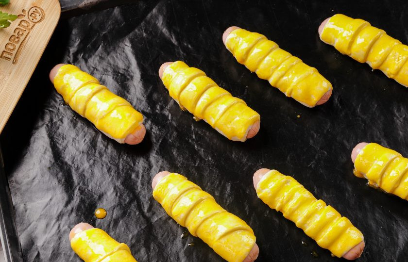 1. Этап. Сосиски в слоеном бездрожжевом тесте в духовке: Выложите сосиски на противень, застеленный пергаментом или специальным кулинарным ковриком. Смажьте тесто взбитым желтком и выпекайте в заранее разогретой духовке при температуре 180 градусов около 15-20 минут.