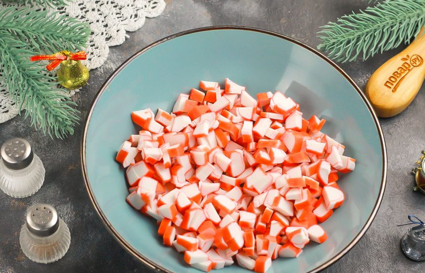 1. Этап. Крабовый салат на Новый год 2025: Крабовые палочки очистите от целлофановой оболочки и нарежьте небольшими кубиками. Высыпьте нарезку в салатник или глубокую миску.