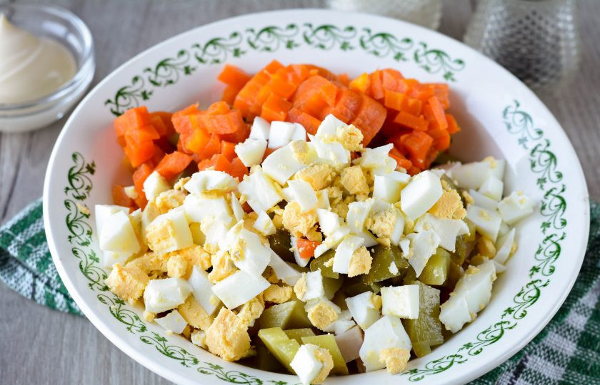 1. Этап. Салат с карбонатом: Отварите морковку до мягкости и нарежьте кубиками. Также сварите яйца вкрутую, остудите и нарежьте кубиками. Добавьте морковку и яйца в салат.