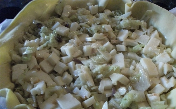 1. Этап. Капустник-пирог: Форму для выпечки диаметром 24 см покройте пергаментной бумагой, выложите на нее круглый пласт песочного теста. Сверху уложите начинку и кубики сыра.