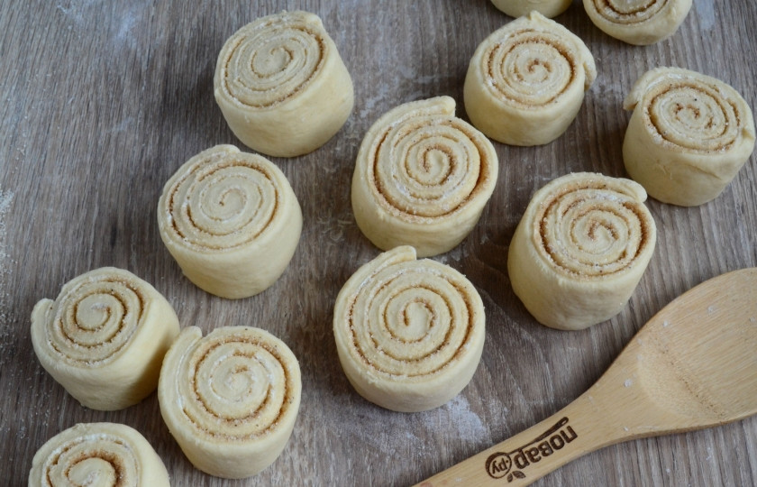 1. Этап. Булочки Синнабон (правильный рецепт 100%): Теперь нужно разрезать этот большой рулет на небольшие кусочки, шириной примерно 4-5 см. Ножом резать не очень удобно, поэтому советую воспользоваться обычной нитью. Возьмите небольшой кусок нити. Запустите его под рулет, поднимите края и перекрестив их, протяните. Таким образом у вас получится ровный и красивый разрез. Так разрежьте весь рулет.