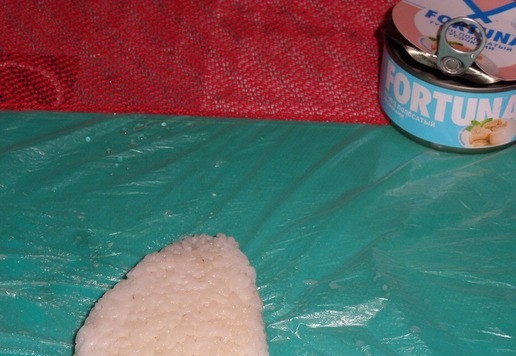 1. Этап. Закуска из риса А-ля Онигири: Приподнимая края пленки, закрываем рыбную начинку. Придаем форму треугольника.