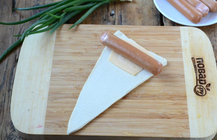 1. Этап. Закуска Крабик: Каждый треугольник слегка растяните в длину. На каждый положите по тонкому ломтику сыра. Сверху положите сосиску. Края сосиски слегка надрежьте.