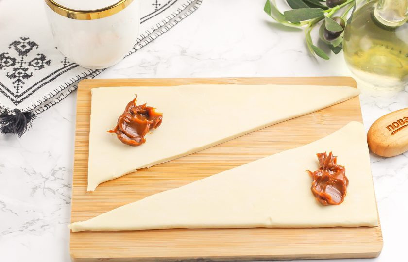 1. Этап. Круассаны в аэрогриле: На широкий края треугольников выложите по 1/2 ст.л. вареной сгущенки или любой другой сладкой начинки. Много не выкладывайте, потому что в процессе выпекания тесто сдавит начинку и она может вытечь за края изделия.