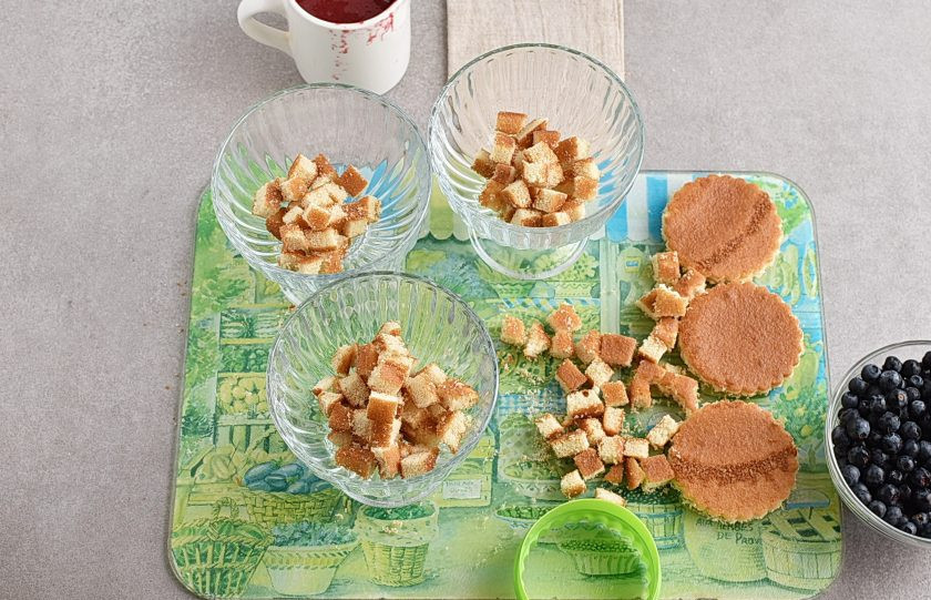 1. Этап. Десерт из мороженого: Формочкой для печенья вырежьте из бисквита три кружочка подходящего к вашим креманкам размера. Остатки нарежьте мелкими кубиками.