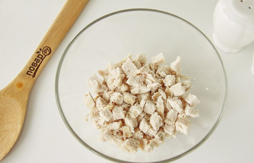 1. Этап. Салат Коралл: Нарежьте отварное куриное филе небольшими кубиками и сложите в глубокую миску или салатник.