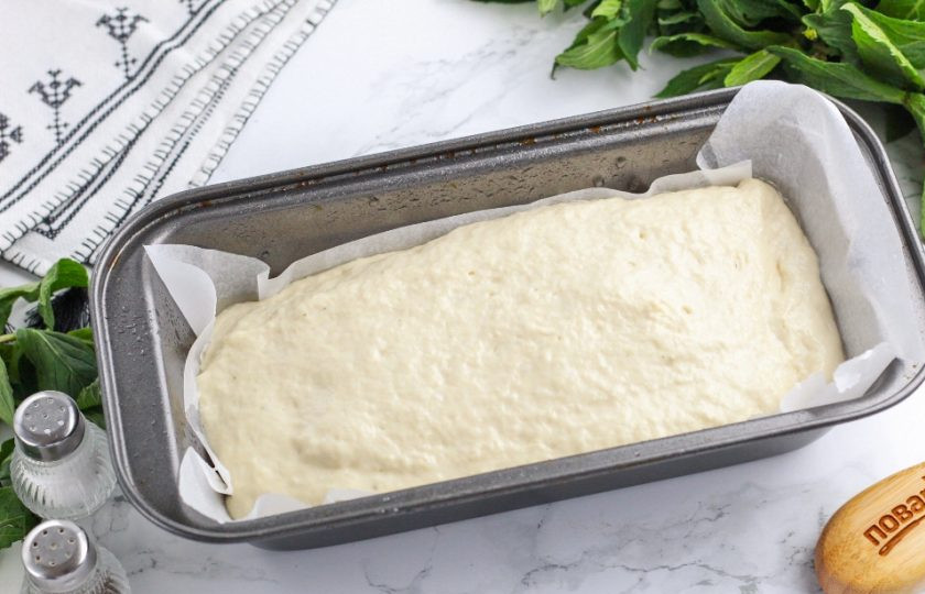 1. Этап. Хлеб в духовке: Выстелите форму пергаментной бумагой и сбрызните ее растительным маслом. Выложите тесто в форму и слегка округлите. Накройте полотенцем и дайте расстояться 20-40 минут в зависимости от температуры в комнате.