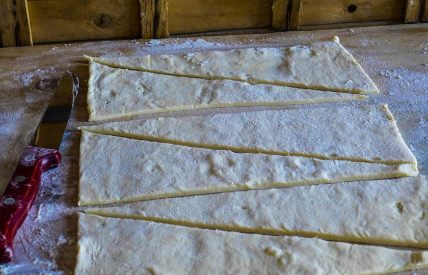 1. Этап. Круассаны с начинкой: Присыпьте стол мукой, выложите слоенное тесто на него и разрежьте на треугольники как на фото.