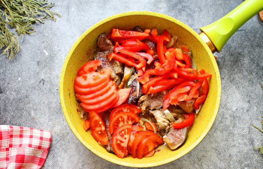 1. Этап. Говяжьи губы с овощами: Болгарский перец порежьте крупной соломкой, помидоры полукольцами. Выложите овощи в сковороду с губами и овощами. Все посолите, поперчите и влейте воду.