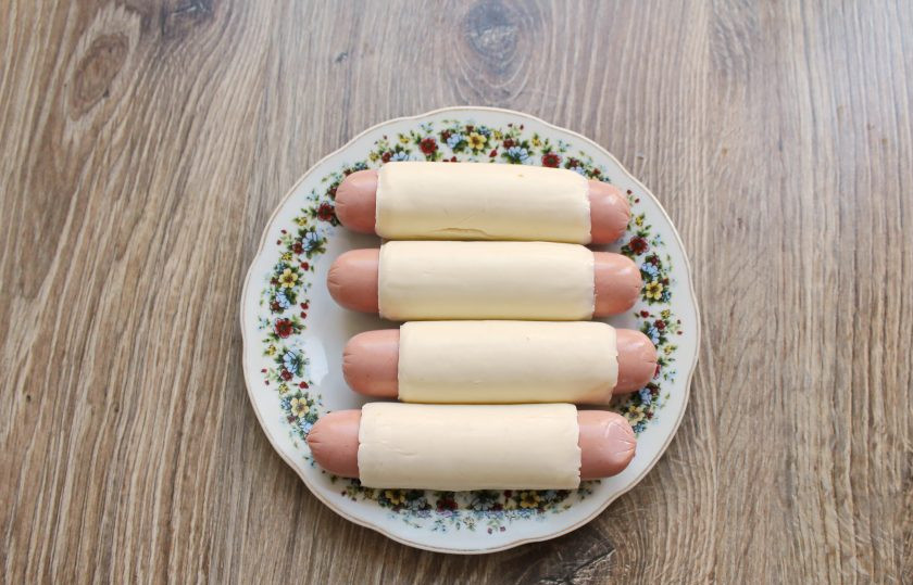 1. Этап. Сосиски в панировке с сыром: Сосиски и сыр очистите от оболочки. Обверните сыр вокруг сосиски, плотно прижимая.