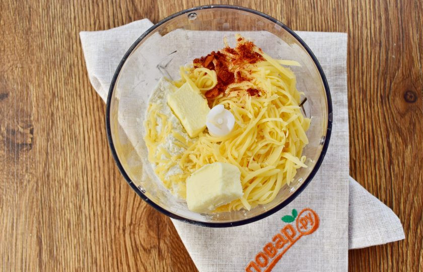 1. Этап. Сырные крекеры-рыбки: Чеддер натрите на мелкой терке. Поместите сыр, сливочное масло, муку, паприку и соль в чашу измельчителя.